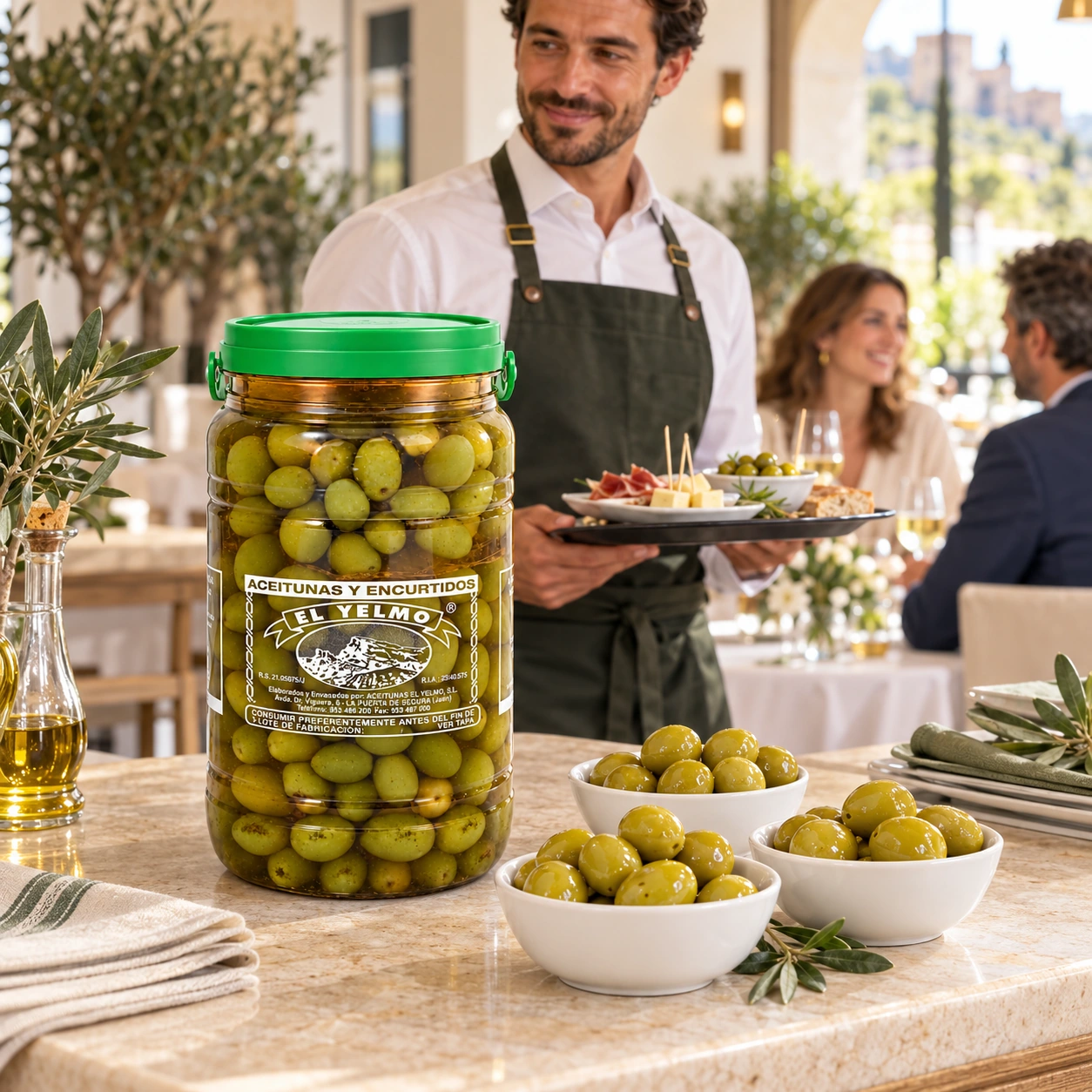 Envase grande de aceitunas Sosa El Yelmo con cuencos de aperitivo, un camarero y comensales en un restaurante.